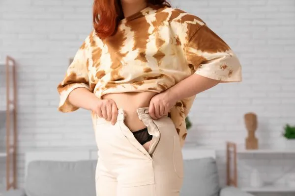 Image of woman trying to do her trousers up after pregnancy weight gain Middlesex