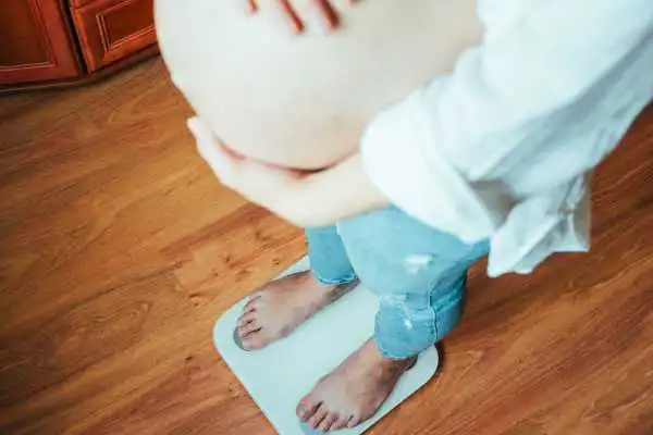 Image of woman weighing herself and experiencing weight gain through pregnancy Middlesex